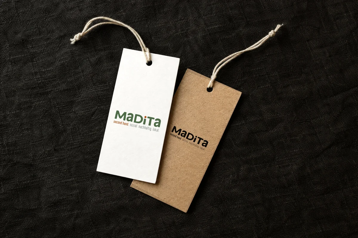 Mockup: zwei Hängeetiketten, weiß mit farbigem Madita-Logo und aus Kraftpapier mit der schwarzen Logovariante.