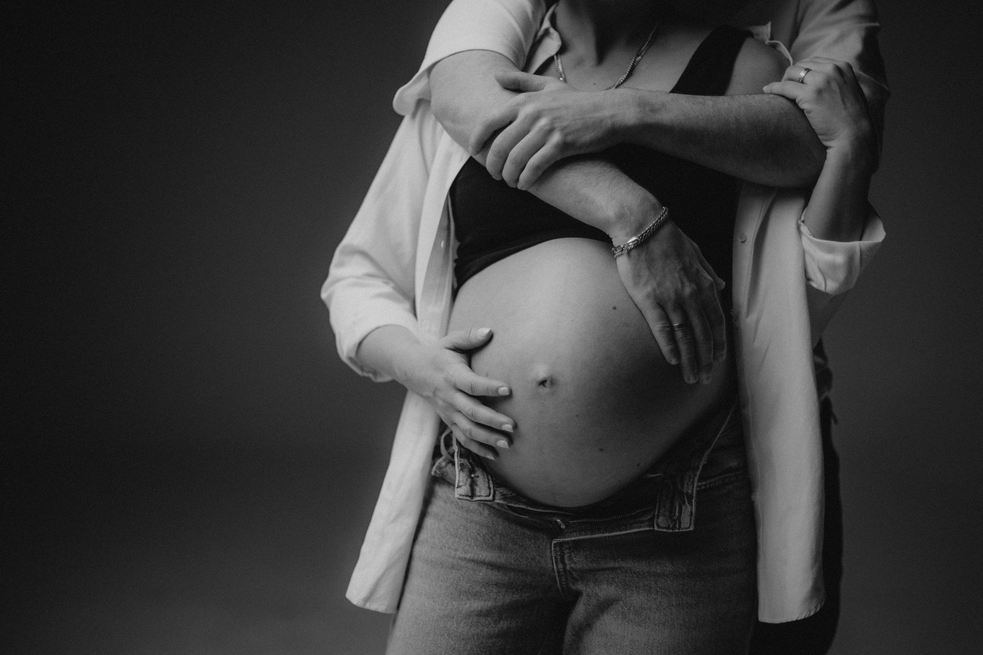 Schwangerschaftsporträt in Schwarzweiß: Hände eines Paares am Babybauch.