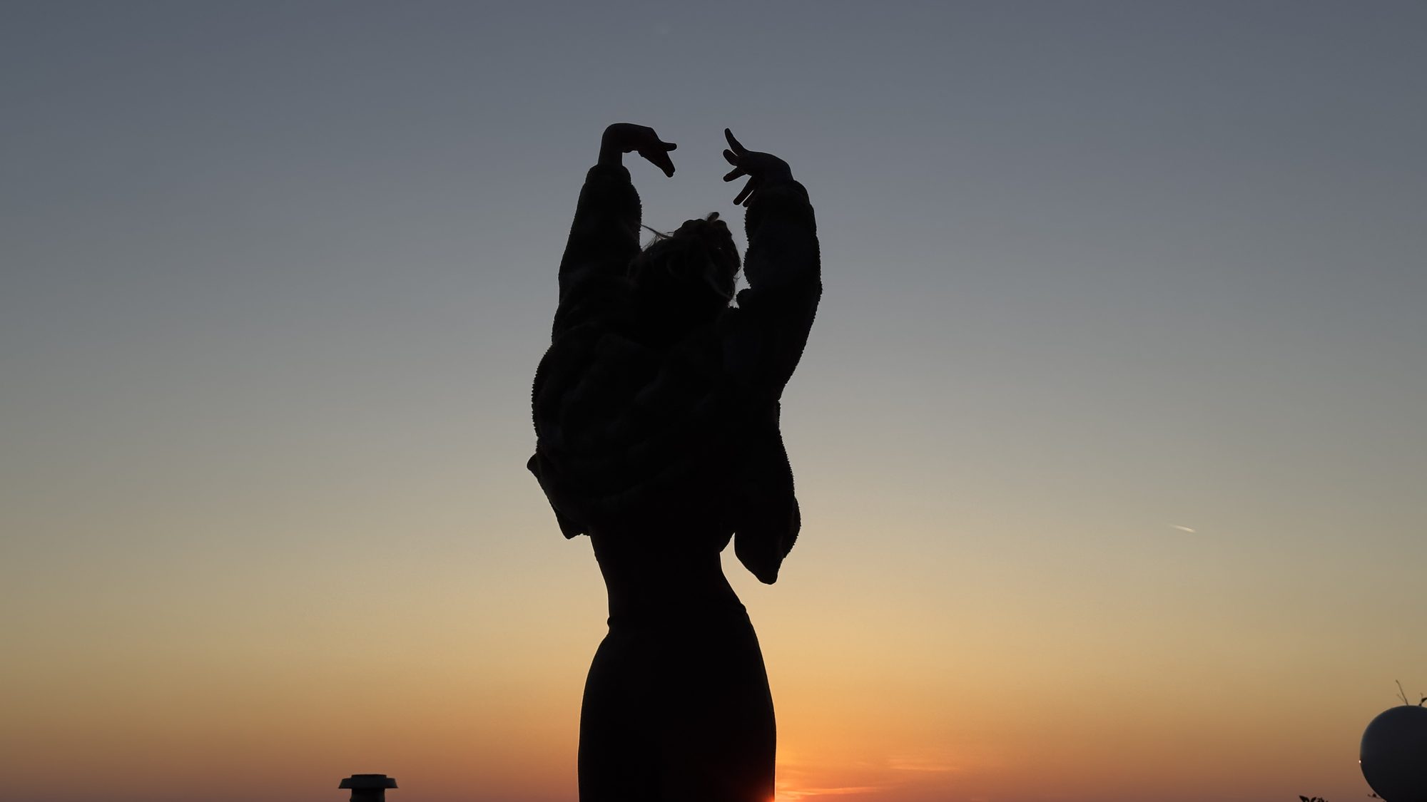 Silhouette einer Frau mit erhobenen Armen vor dem Abendhimmel nach Sonnenuntergang.